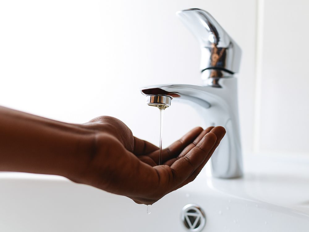 Hand under faucet with a very weak trickle of water flowing out, illustrating how sediment from a dirty tank can cause low pressure and clogs.